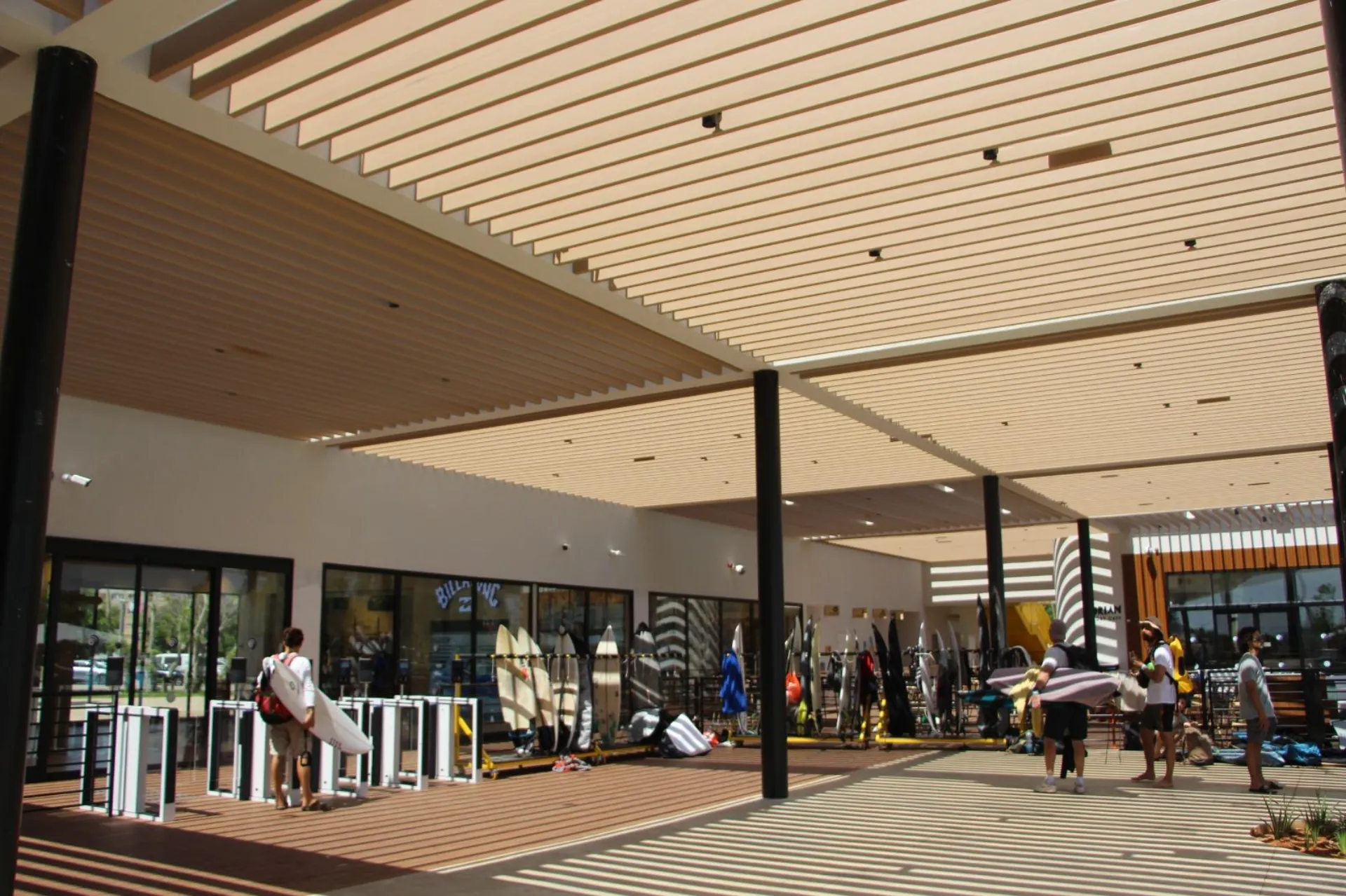 Wood-look aluminum slatted pergola and trellis ceiling over a commercial walkway casting patterned shade