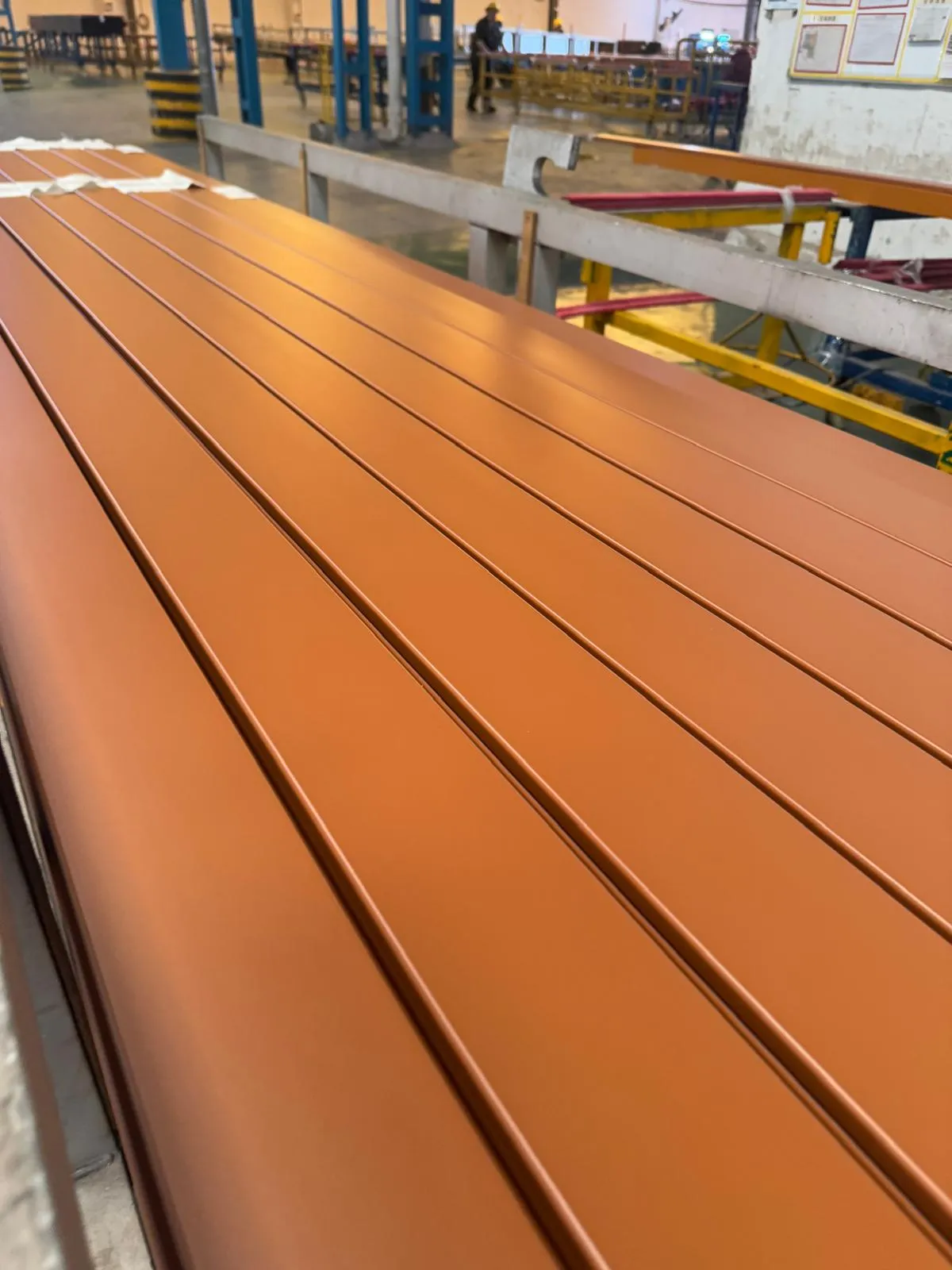 Aluminum siding extrusions in solid powder-coat finish on the factory line before the sublimation wood-grain transfer step